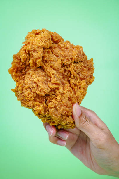 istock Female hand holding fried chicken on green background. 2113156299
