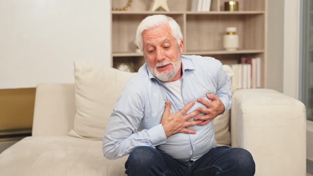 Pain on heart, heart attack. Unhappy middle aged senior man suffering from chest pain heart attack problems with health at home. Mature old senior grandfather touching chest experiencing infarction.