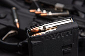 Close-up of .223 carbine cartridges. Loaded weapon clip. Weapons in the background.