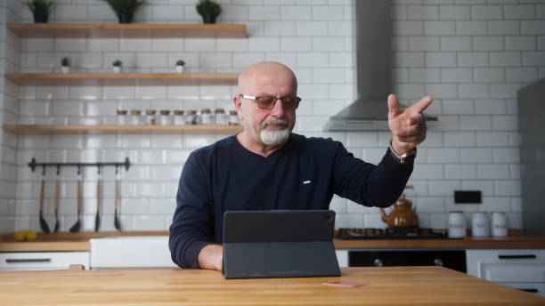 Elderly man sit in kitchen enter credit card number on tablet and due insufficient funds experiencing problems during payment online with credit card get mad Elderly man sit in kitchen enter credit card number on tablet and due insufficient funds experiencing problems during payment online with credit card get mad insufficient funds stock pictures, royalty-free photos & images