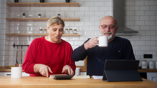 Old couple sit in kitchen doing paperwork, checking calculating bills bank loan payment, discuss unpaid debt taxes. Old grandparents family money problem concept