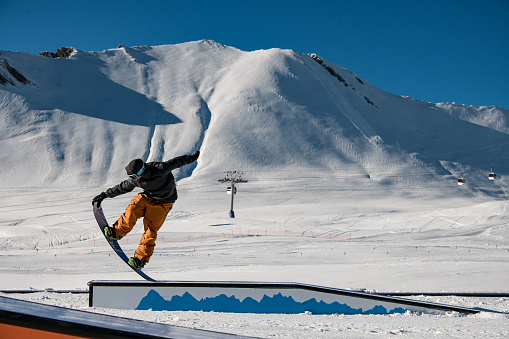 The snowboarder displays wallride elegance, performing a seated trick and balancing with precision on the slope.