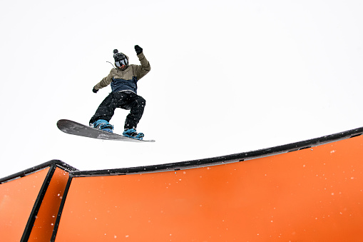 Skilled snowboard pro masters a jump into a wallride, navigating a challenging slope effortlessly.