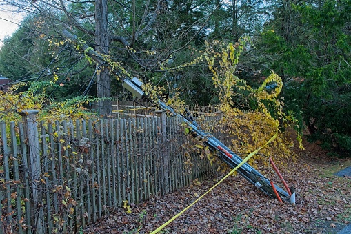 Downed wooden utility pole against picket fence with surrounding yellow caution tape