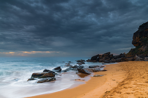 Cloudy sunrise seascape with waves and rocks at Killcare Beach on the Central Coast, NSW, Australia.