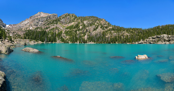 A panoramic view of colorful Lake Haiyaha, with Hallett Peak towering at shore, on a sunny and calm Summer day. Rocky Mountain National Park, Colorado, USA.