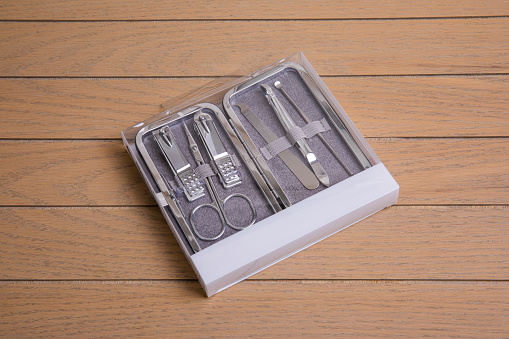 multi-piece metal nail tool kit in transparent plastic packaging with metal box on wooden background overhead view