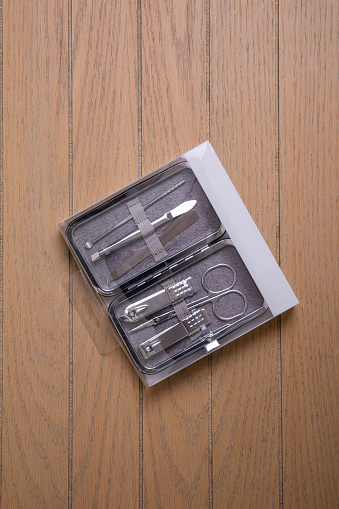 multi-piece metal nail tool kit in transparent plastic packaging with metal box on wooden background overhead view