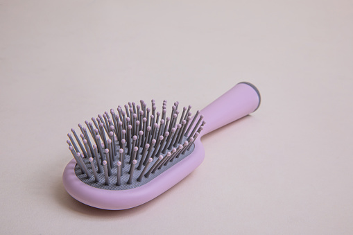 pink plastic comb with handle with gray details on a beige background