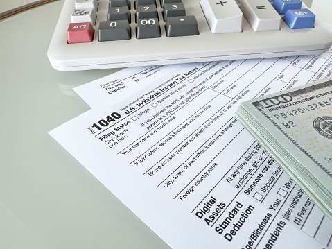 Looking down on 1040 tax forms and dollar bills with calculator on table top