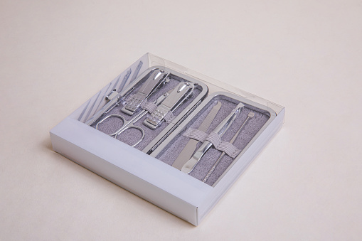 multi-piece metal nail tool kit in transparent plastic packaging with metal case on beige background