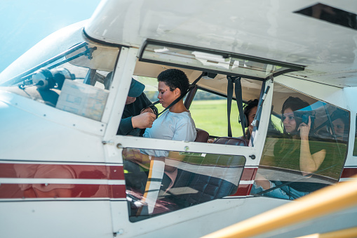 A diverse group of tourists, both male and female, are seated inside a small aircraft, wearing headphones, and looking out the windows, preparing for a scenic flight experience.
