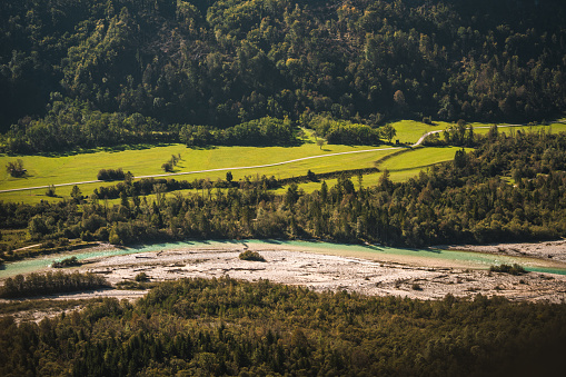 The image captures an aerial panorama of a vibrant green landscape with light dancing on a riverbed, framed by dense forested hills.