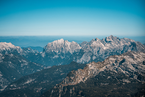 A panoramic aerial shot capturing the rugged beauty of a mountain range under a clear blue sky.