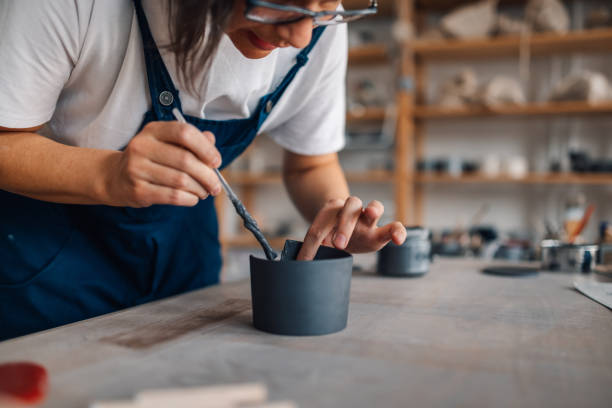 Close up of craftswoman's hands using pottery tool and molding a mug.