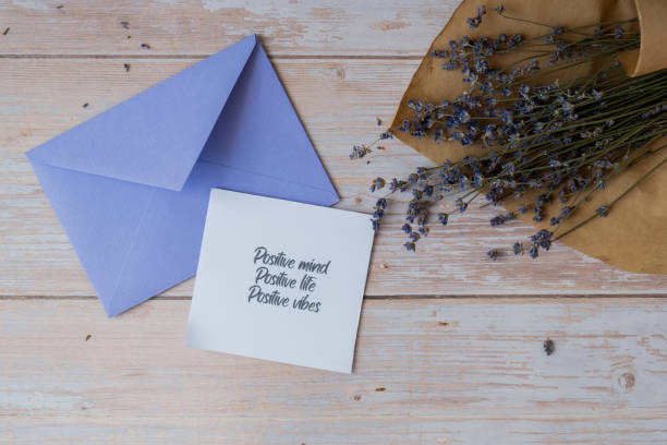 POSITIVE MIND LIFE VIBES text on supportive message paper note reminder from violet envelope. Flat lay composition dry lavender flowers. Concept of inner happiness, slowing-down digital detox personal fulfillment. Top view