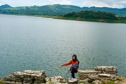 An Asian woman is on a road trip in a body of water that has steep terrain.