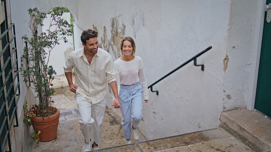 Enamoured pair stepping staircase at south city. Unshaven macho man looking woman tenderly. Happy couple holding hands at tiny town. Sweethearts enjoying romantic time. People relationships concept