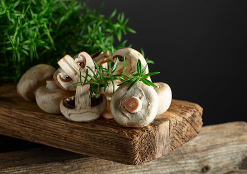 White champignons with rosemary on an old wooden board.