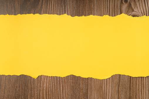 Piece of yellow torn paper on a wooden background. Space for text.