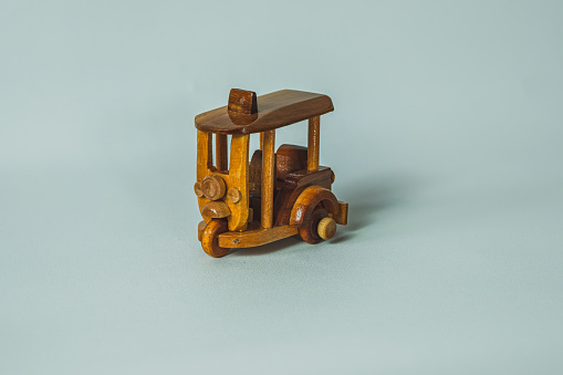 A close-up photo of a simple, wooden toy car called tuk tuk on a flat, white background.