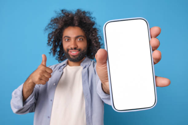 istock Young joy optimistic Arabian man with smartphone in hand showing thumbs up 2113886664