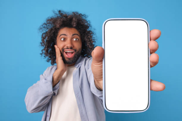 istock Young surprised positive Arabian man with mobile phone with white screen 2113887185
