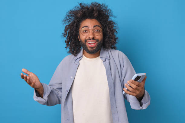 istock Young inspired Arabian man with phone happily spreads hands stands in studio 2113887694