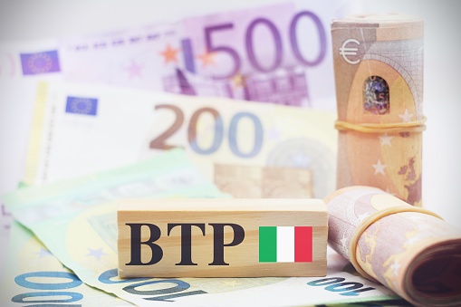 European banknotes with wooden cubes and Table with european banknotes as background with the text BTP translating as Italian government bonds.