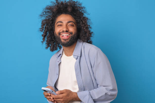 istock Young Arabian man student laughing holding mobile phone stands in studio 2113888209