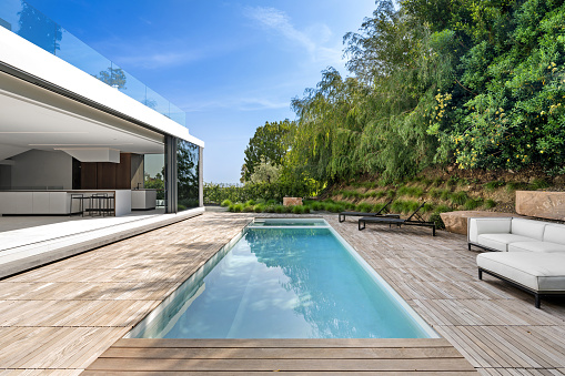 Magnificent view of a swimming pool standing in a garden, with multiple trees and mountains in the background, on a sunny day