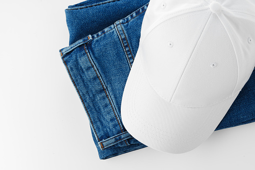 A pair of blue jeans and a baseball cap are placed neatly on a plain white background.