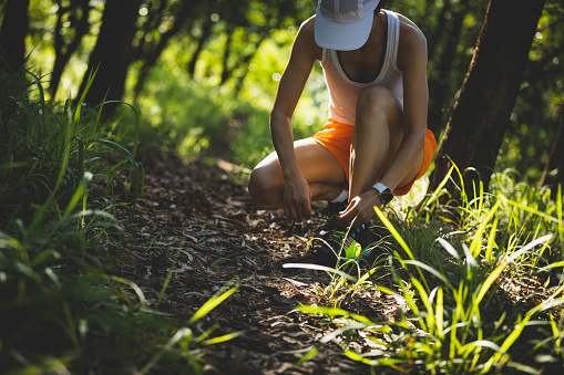 Woman runner tying shoelace on forest trail