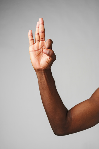 Human Hand Gesturing Three Fingers Up Against a Neutral Grey Background close up