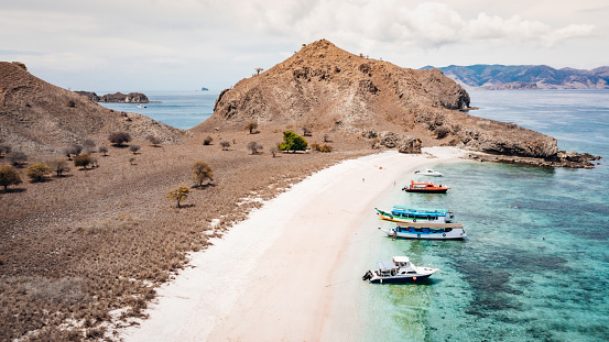 Pink Beach Padar Island in the Komodo Island National Park with anchored indonesian Tourboats. Aerial Drone view along the famous Pink Beach in the Komodo National Park. Natural pink colored beach towards clean coral reef water. Padar Island, Komodo National Park, Komodo island, Labuan Bajo, Flores, Indonesia, Southeast-Asia.