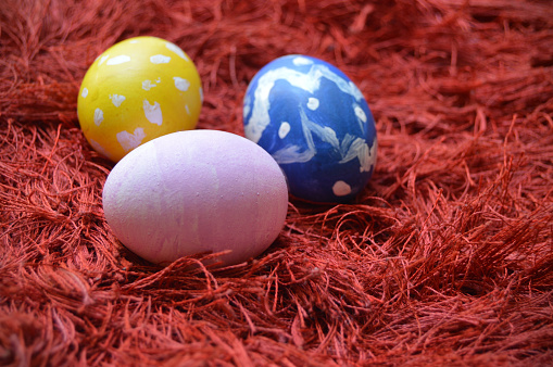 Colorful hand painted Yellow, blue and pink ornate Easter eggs on bright vibrant red maroon carpet or rug background for of Easter holidays celebration with copy space