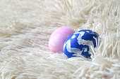 Colorful hand painted two blue and pink ornate Easter eggs on bright off white cream colored fur or furry fleece carpet or rug background for of Easter holidays celebration with copy space