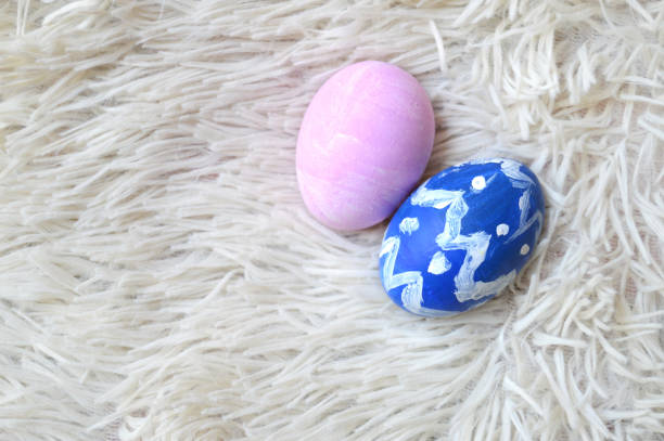 Colorful hand painted two blue and pink ornate Easter eggs on bright off white cream colored fur or furry carpet or rug background for of Easter holidays celebration with copy space. Apt for use as greeting cards, posters and backdrops.