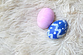 Colorful hand painted two blue and pink ornate Easter eggs on bright off white cream colored fur or furry carpet or rug background for of Easter holidays celebration with copy space