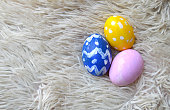 Colorful hand painted Yellow, blue and pink ornate Easter eggs on bright off white cream colored fur or furry carpet or rug background for of Easter holidays celebration with copy space