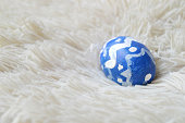 Single hand painted one blue ornate Easter egg on bright off white cream colored fur or furry carpet or rug background for of Easter holidays celebration with copy space