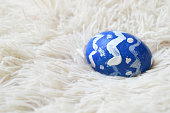 Single hand painted one blue ornate crafted Easter egg on bright off white cream colored fur or furry carpet or rug background for of Easter holidays celebration with copy space