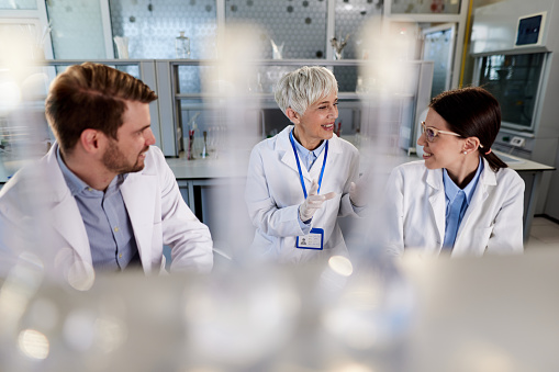 Happy teacher of chemistry and her young students talking while working on medical research in laboratory. Copy space.