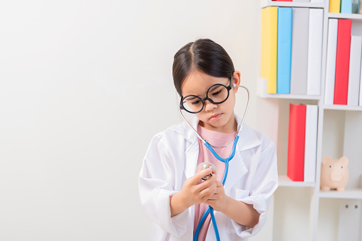 Cute little girl asian with stethoscope playing doctor, wear medical uniform and glasses, holding stethoscope playing doctor,