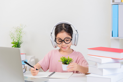 Online Education. Cute little Girl asia Study At Home With Laptop And Wireless Headphones, Adorable Kid Having Web Lesson With Teacher, Enjoying Distance Learning During Quarantine Time, Free Space