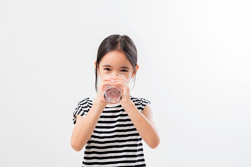 cute little asian girl Standing and Smiling little with a holding an empty glass of water on white background