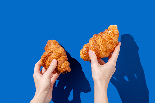 Women's hands hold fresh croissants on a blue background. Design concept for breakfast pastry mockup or banner. Free space fot text.