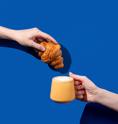 Women's hands hold fresh croissant and cup of coffee  on a blue background. Design concept for breakfast pastry mockup or banner. Free space fot text.