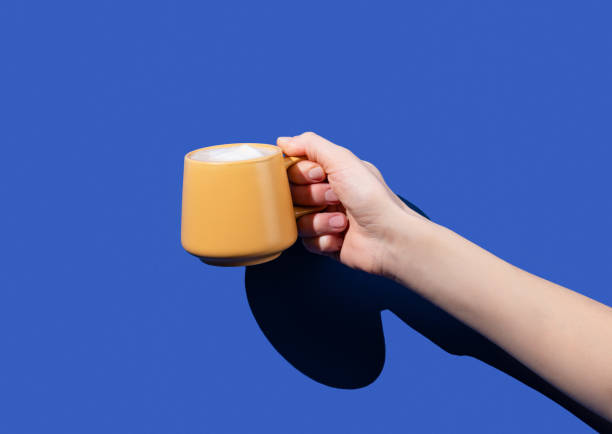 istock Hand hold yellow cup coffee on a blue background. Design concept for breakfast pastry mockup or banner. 2114006792