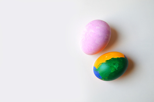 Two colorful hand painted pink and multi colored green blue and yellow ornate Easter eggs on bright off white cream colored background for of Easter holidays celebration with copy space. Apt for use as greeting cards, posters and backdrops.